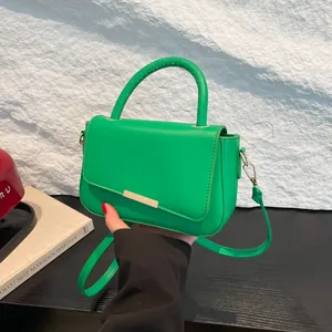 Sac à main vert vif pour femme avec boucle dorée et bandoulière sur un fond texturé blanc