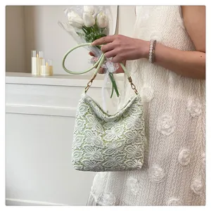 Detail of light green lace tote bag with white floral patterns and gold metal buckles