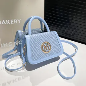 Borsa a mano azzurra con pannello intrecciato e logo M dorato su espositore bianco