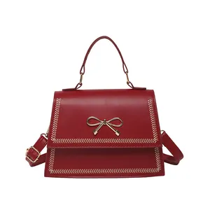 Elegante bolso bandolera rojo con cierre de lazo dorado y costuras decorativas en V