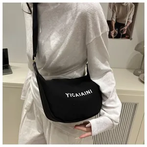 Vue détaillée du sac bandoulière en toile noire avec lettrage blanc et sangle réglable