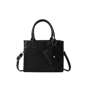 Black leather crossbody square bag with top handle and mini pouch charm on white background