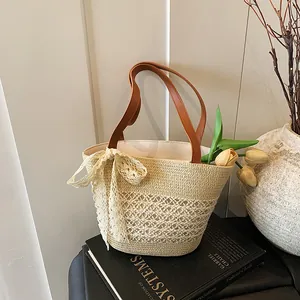 Chic straw woven bucket bag with brown leather handles and white lace bow for beach