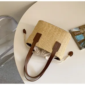 Detail of hand-woven straw tote bag with brown leather handles and interior drawstring