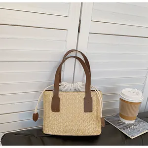Close-up of woven straw tote with brown leather handles and white drawstring liner