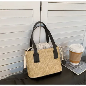 Detail of hand-woven straw tote bag featuring black leather handles and drawstring liner