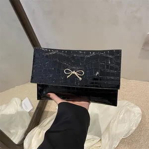 Elegant black crocodile pattern envelope clutch with a gold bow buckle on white fabric