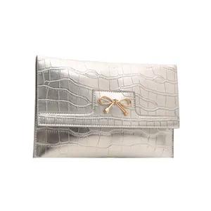 Silver croc-embossed square handbag with a decorative golden metal bow on white background