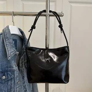 Glossy black patent leather tote bag with silver bow accent on a hanger with denim