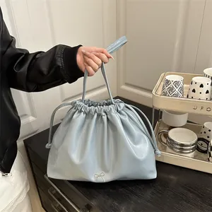 Chic light blue drawstring bucket bag with silver bow accent in a soft leather finish