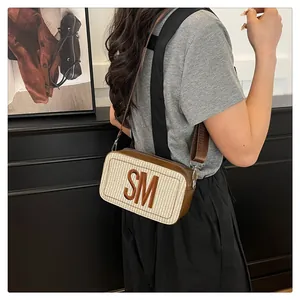 Detail einer Stroh-Umhängetasche mit braunem SM-Patch und breitem Nylon-Schultergurt