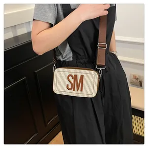 Detail der beigen Stroh-Umhängetasche mit SM-Stickerei und breitem braunem Gurt