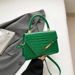 Groene crossbodytas met krokodillenreliëf, goudkleurige bies en rond handvat op blazer