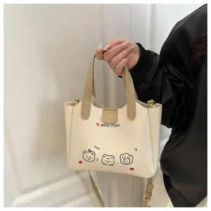 Détail du sac cabas crème avec motif ours, anses kaki et finitions métalliques dorées
