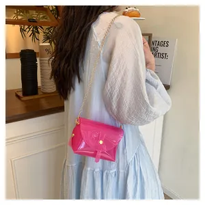 Détail d'un sac enveloppe rose transparent avec bandoulière dorée porté par un mannequin