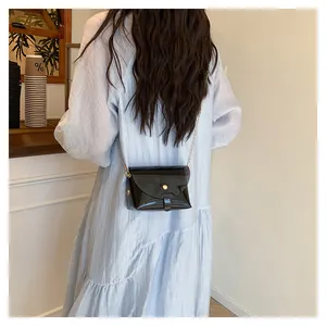 Détail du sac enveloppe en cuir verni noir avec fermoir doré sur robe rayée