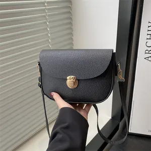 Minimalist black pebble leather saddle bag with gold lock shown in a stylish indoor setting