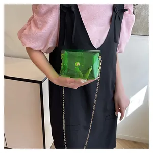 Détail du sac enveloppe transparent vert avec chaîne dorée porté par un mannequin