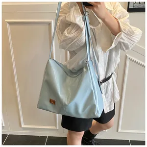 Detail of light blue glossy tote bag with gold metal plate and adjustable strap on model