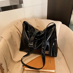 Fashionable black glossy underarm tote bag with silver buckle on a beige sofa