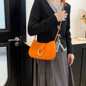 Borsa a sella in pelle arancione con fibbia a U dorata, indossata da una modella chic