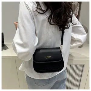 Close-up of black leather saddle bag with gold logo text and woven embossed texture details