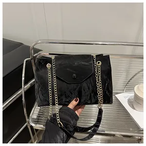 Macro detail of the black pleated texture and shiny gold chain strap of the shoulder bag