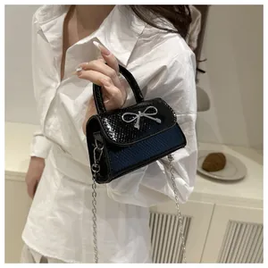 Detail of black snake pattern faux leather shoulder bag with silver metal bow and chain