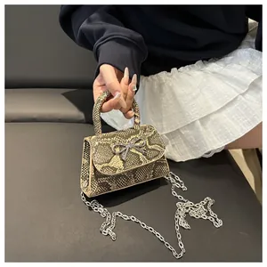 Close-up of snake skin crossbody bag with silver bow clasp and chain strap detail