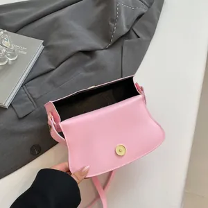 Pink semi-circular shoulder bag with gold magnetic buckle on a grey blazer backdrop