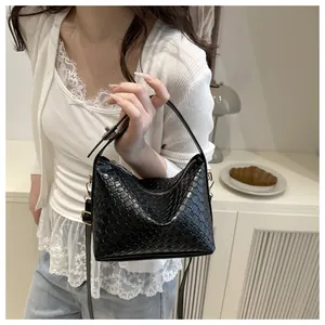 Détail de la texture tressée noire du sac à main avec finitions dorées et bandoulière