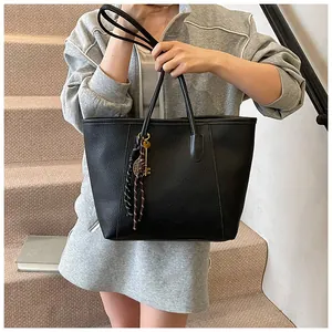Detail of black pebbled leather tote bag featuring metal key charm and woven knot decor