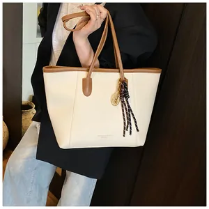 Detail of cream tote bag with brown handles, tennis racket charm, and decorative scarf