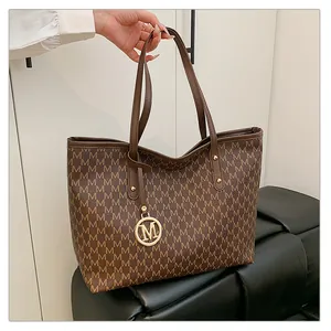 Gros plan détaillé d'un sac cabas marron avec motifs M et pendentif doré rond