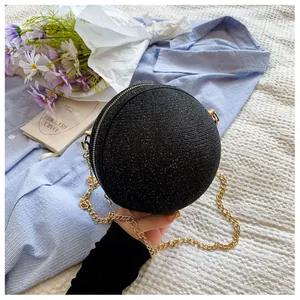 Sparkling black round ball evening bag with gold chain strap on a textured bed