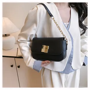 Detail of a black leather crossbody bag with a gold buckle worn with a white blazer