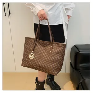 Détail du sac cabas marron foncé avec imprimé M et breloque logo dorée sur la poignée