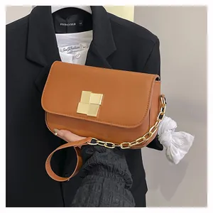 Detailed view of brown leather crossbody bag featuring a golden interlocking metal buckle