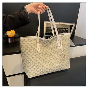 Détail d'un cabas beige à monogramme avec pendentif M doré dans un décor de bureau