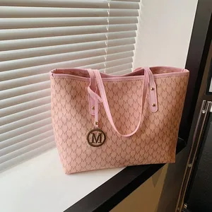 Sac fourre-tout rose avec motif lettres M et pendentif doré devant une fenêtre