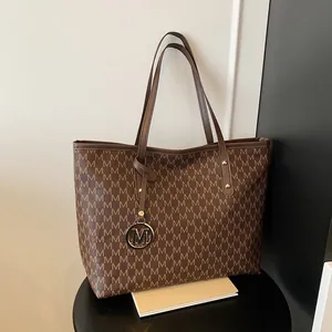 Sac cabas marron avec motif monogramme et pendentif en métal M sur tabouret sombre