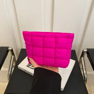 Bright pink quilted puffer cosmetic bag held by hand in a minimalist urban setting