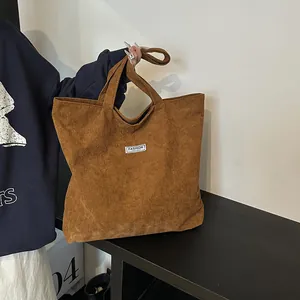 Dettaglio della borsa tote in velluto marrone con trama a coste e toppa con logo