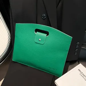 Minimalist green pebble leather commuter handbag displayed on a black blazer with books