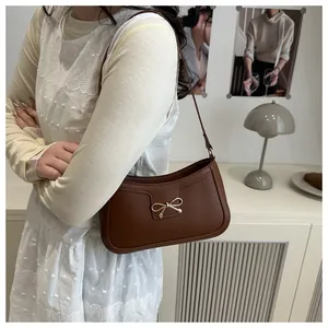 Détail d'un sac à bandoulière marron orné d'un nœud décoratif en métal doré sur le devant