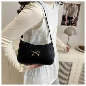 Détail d'un sac porté épaule noir avec un nœud argenté sur cuir synthétique mat
