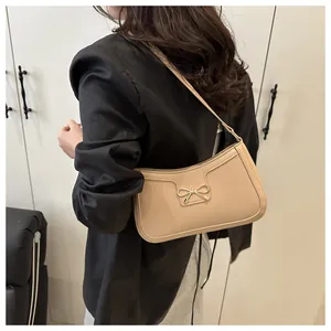 Détail du sac beige avec fermoir nœud doré porté par un mannequin dans un décor épuré