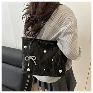 Detail of black tote bag featuring pearl accents and bow-shaped pleated texture