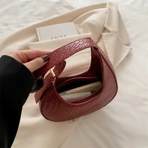 Chic burgundy woven crescent hobo bag with gold zipper held against a neutral blazer