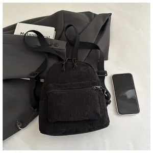 Detailansicht eines schwarzen Cord-Minirucksacks mit Reißverschlussfach auf Stoffhintergrund